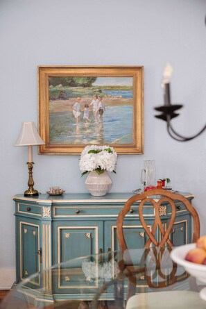 A dining area with a table, chairs, a lamp, a painting, and a cabinet. - Charming 2 BDRM Apt w/ Balcony| Historic District (Savannah)
