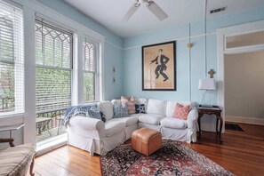 A room with a white sectional sofa, a patterned rug, a ceiling fan, and a large window with blinds. - Charming 2 BDRM Apt w/ Balcony| Historic District (Savannah)