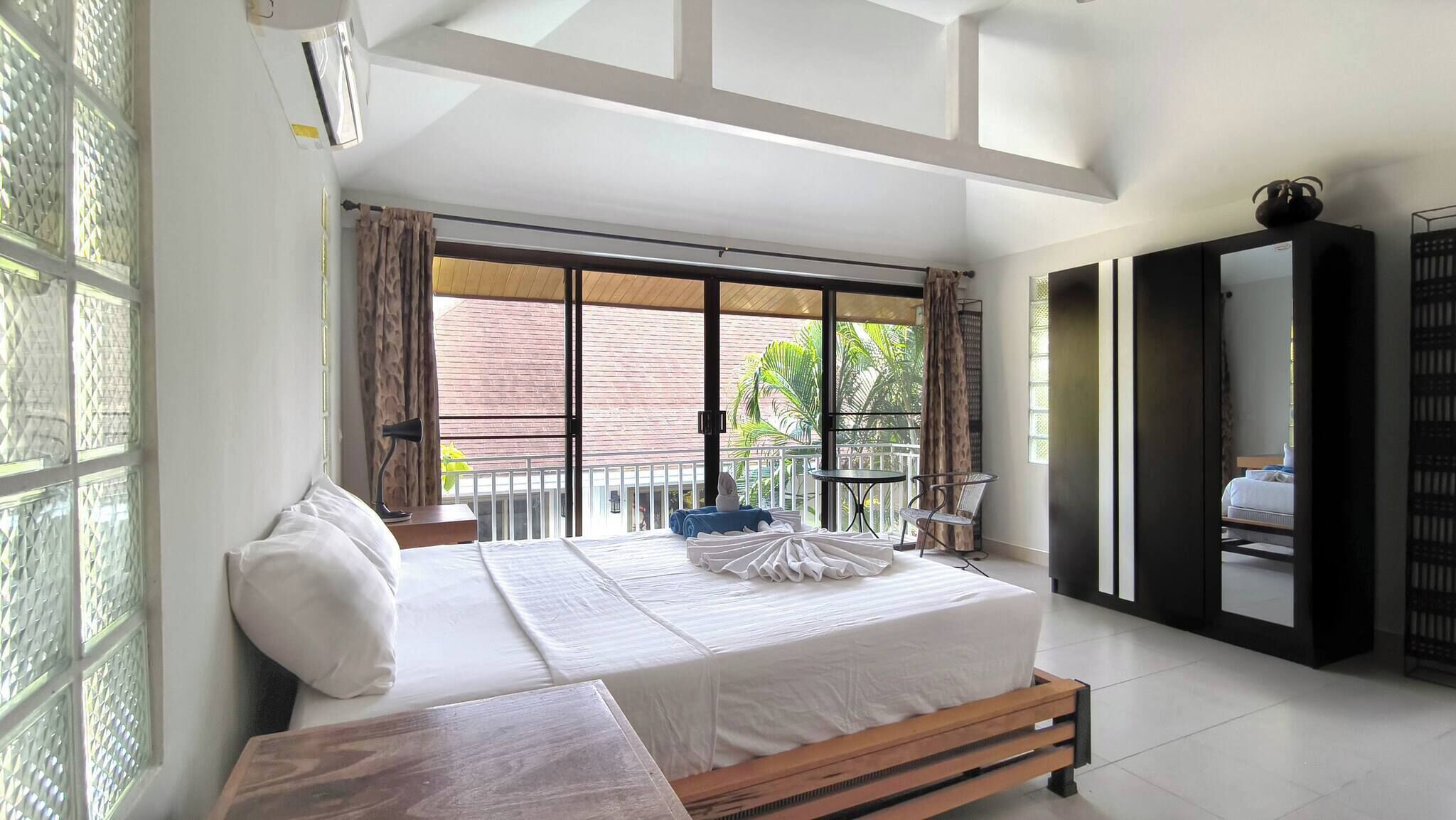 Un dormitorio con una cama grande, un banco de madera, un balcón con vistas y un armario.