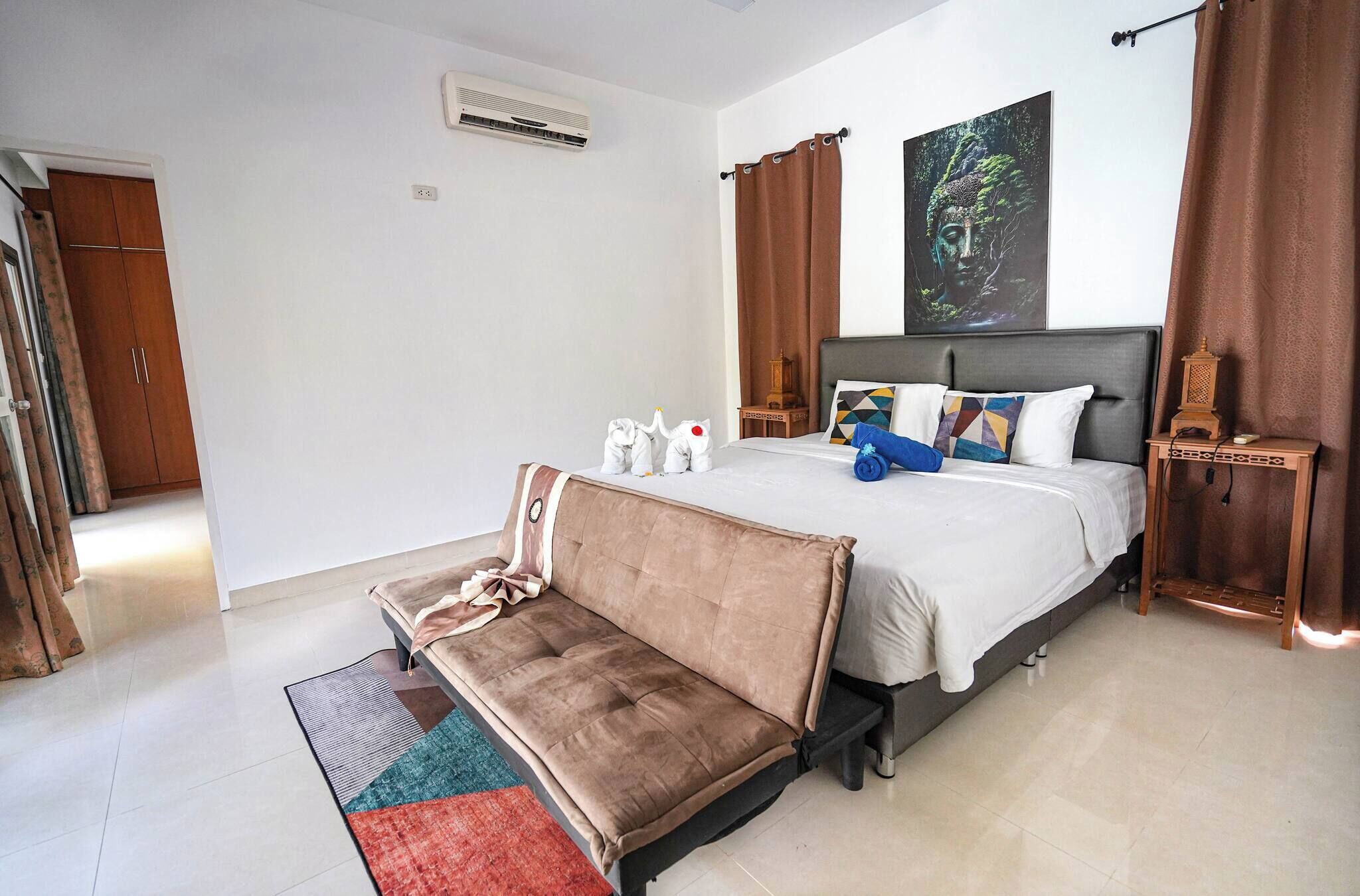 Une chambre à coucher comprenant un lit, un canapé, une table de chevet, un climatiseur fixé au mur et un tableau.
