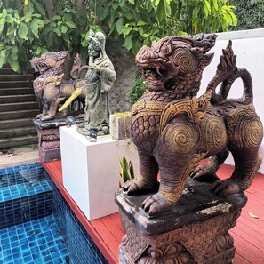 Eine Statue eines mythologischen Wesens mit aufwendigen Schnitzereien, auf einem Sockel in der Nähe eines Pools.