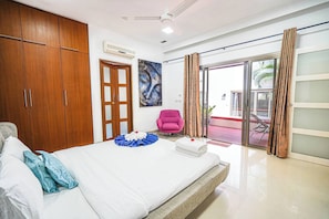 A hotel room with a bed, wooden wardrobe, a pink chair, a painting, and a sliding glass door to the outside. - Kyshia Nai Harn Beach (Rawai)