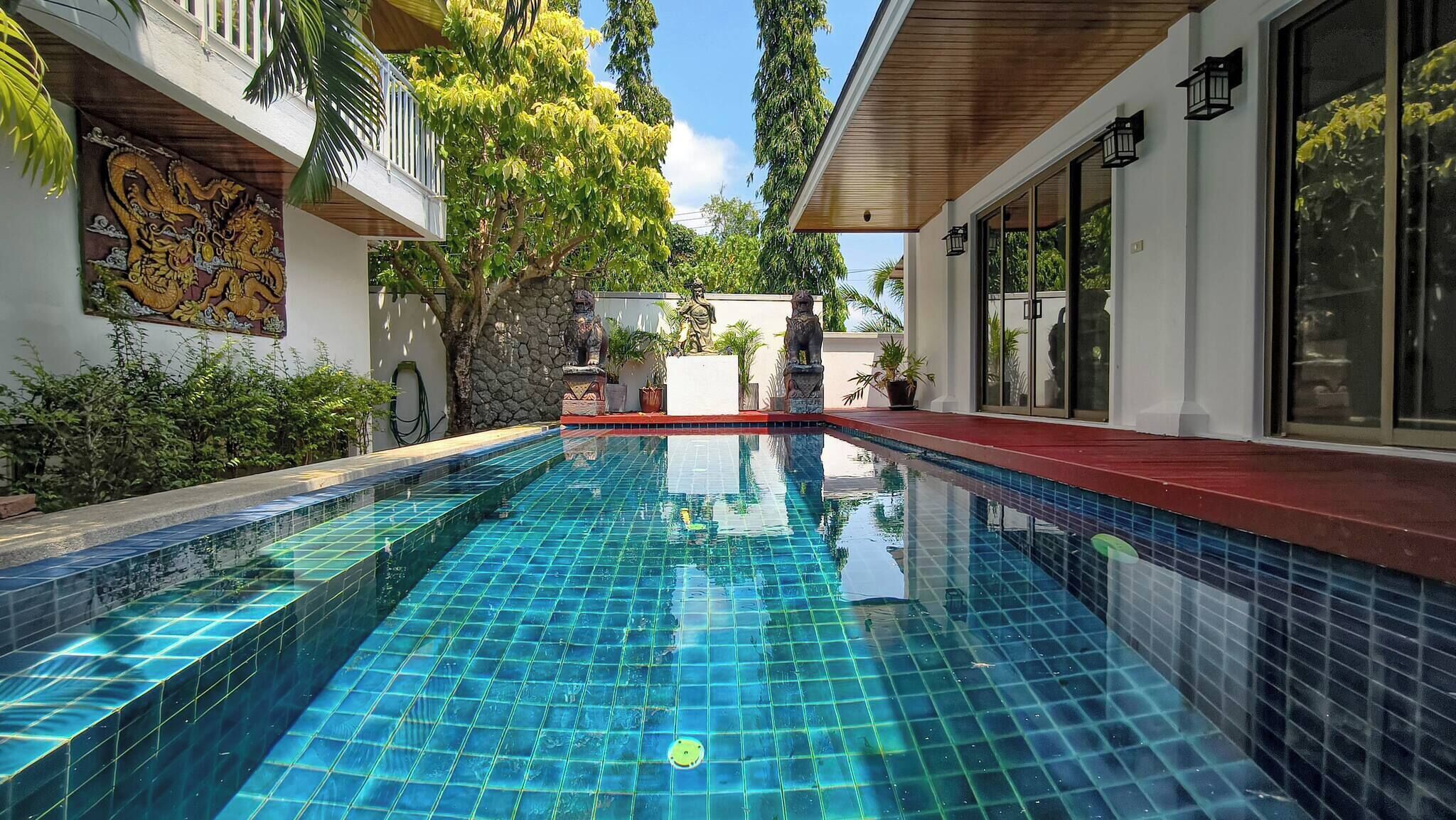 Una piscina con baldosas azules cristalinas, rodeada por un edificio con balcón y decoraciones de pared de piedra.