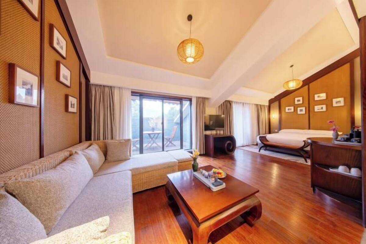 A hotel room with a sofa, a wooden coffee table, a bed, and a TV.