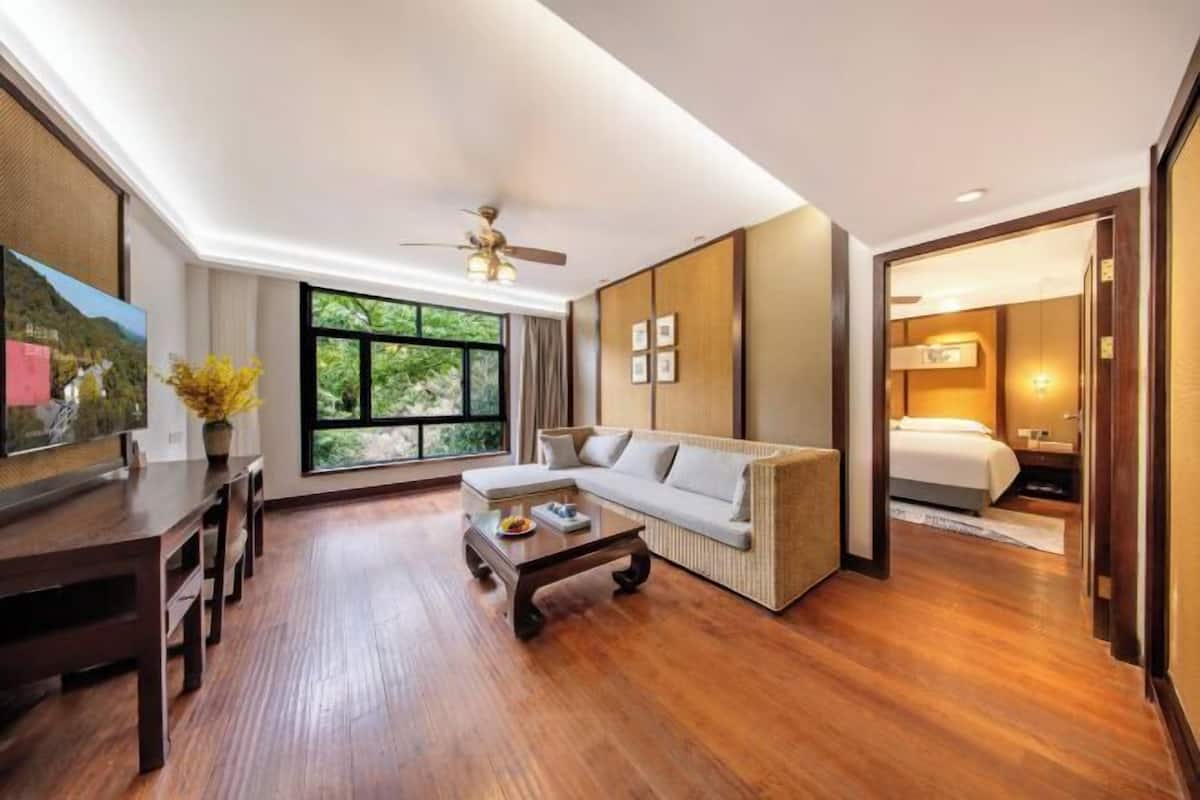 A hotel room with a wooden floor, a sofa, a bed, a desk, and a ceiling fan.