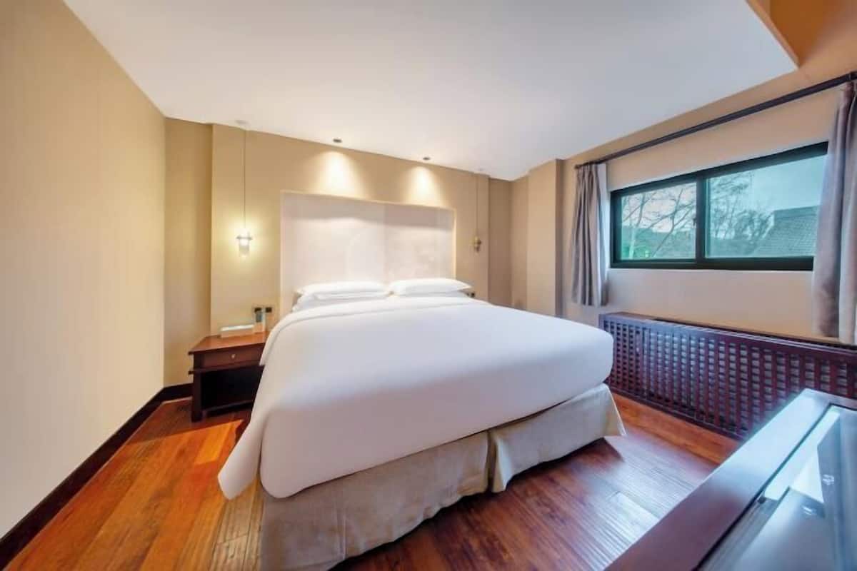 A hotel room with a large bed, a nightstand, a desk, and a window with curtains.