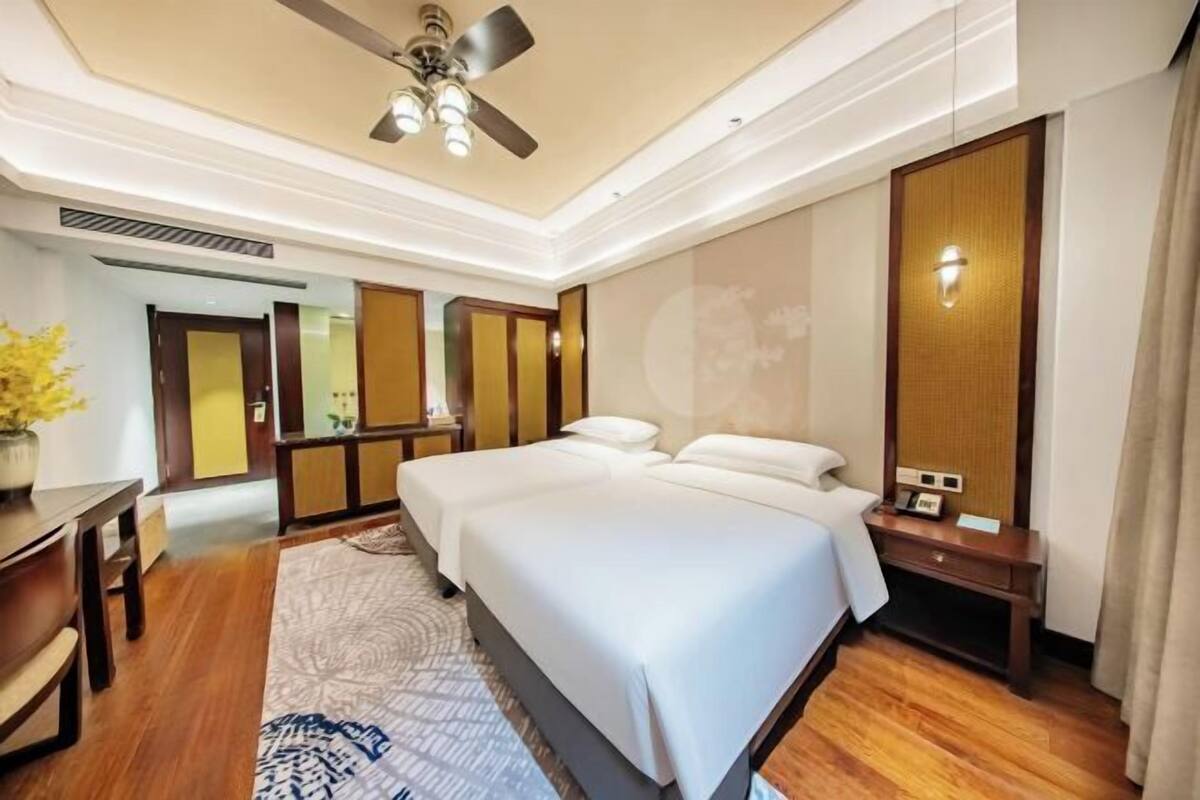 A hotel room with a large bed, a desk, a chair, a ceiling fan, and a wall-mounted TV.