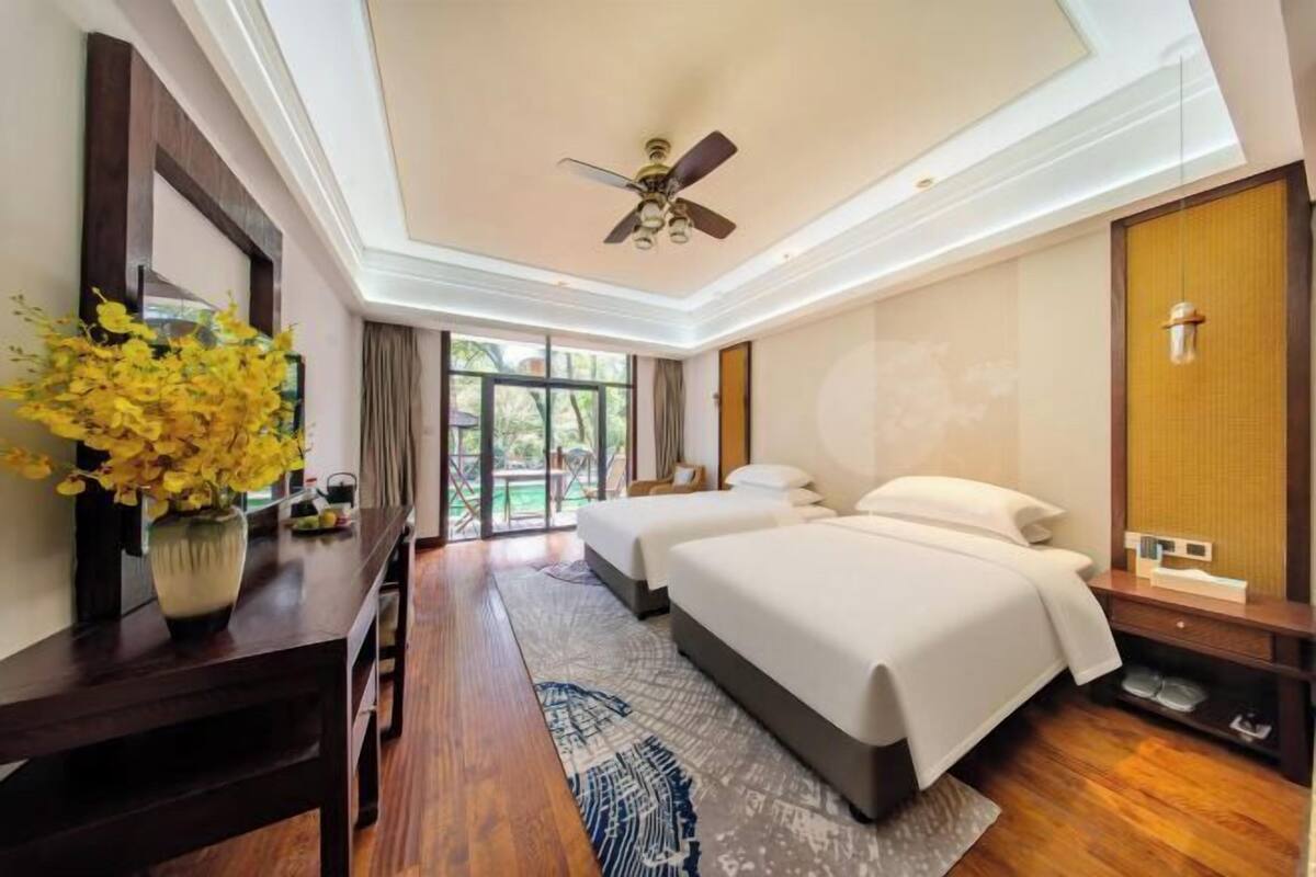 A hotel room with two beds, a ceiling fan, a large window, and a wooden floor.