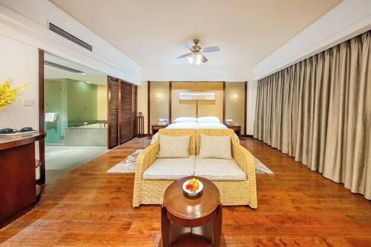 A hotel room with a bed, a sofa, a desk, a ceiling fan, and a view of the bathroom.