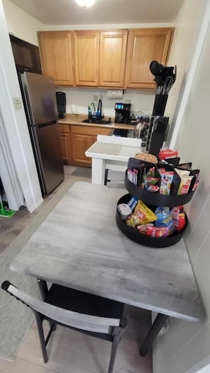 Een kleine keuken met houten kastjes, een koelkast, een koffiezetapparaat en een snoeprek.