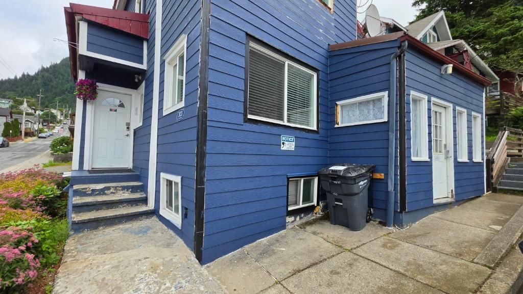 Una casa azul de dos pisos con una puerta blanca, un letrero y un contenedor de basura afuera.