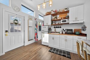 Een moderne keuken met witte kasten, een magnetron, een fornuis en een spoelbak. Er is een houten aanrechtblad en een raam boven de spoelbak.