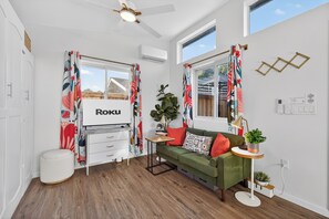 Een moderne woonkamer met een groene bank, een klein tafeltje, een plant en een tv waarop 'Roku' wordt weergegeven.