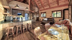 Een rustiek houten huisje van binnen, met een keuken, eethoek en zithoek.