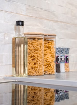 Drei Gläser mit Pasta auf einer reflektierenden Oberfläche vor einer weißen Ziegelwand.