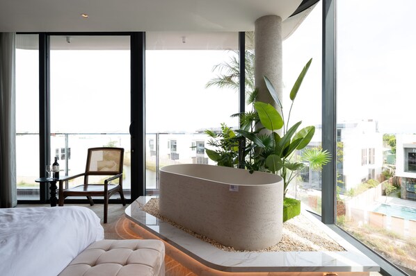 Une chambre d’hôtel moderne dotée d’une grande baignoire, d’un lit, d’une table à manger avec des chaises et d’un balcon offrant une vue sur la ville.