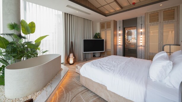 Ett modernt hotellrum med en stor säng, en platt-TV, ett badkar och ett stort fönster med gardiner.