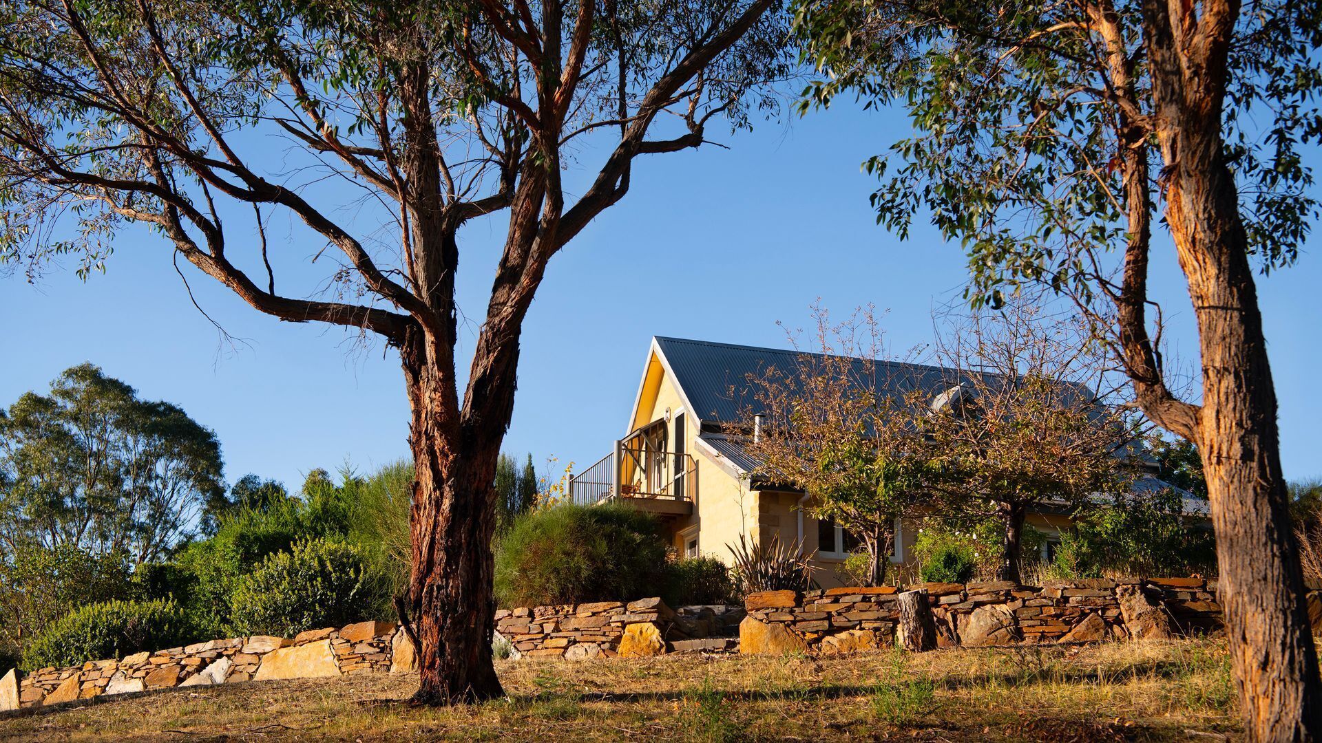 Una casa con un muro de piedra y árboles altos al frente.