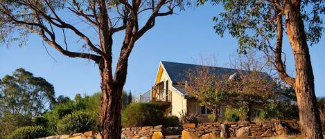 Una casa con un muro de piedra y árboles altos al frente.