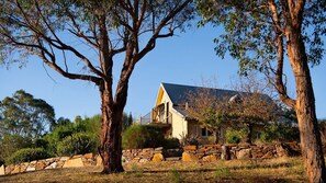 A house with a stone wall and large trees in the foreground. - El Camino Fireplace and Spa (Elevated Plains)