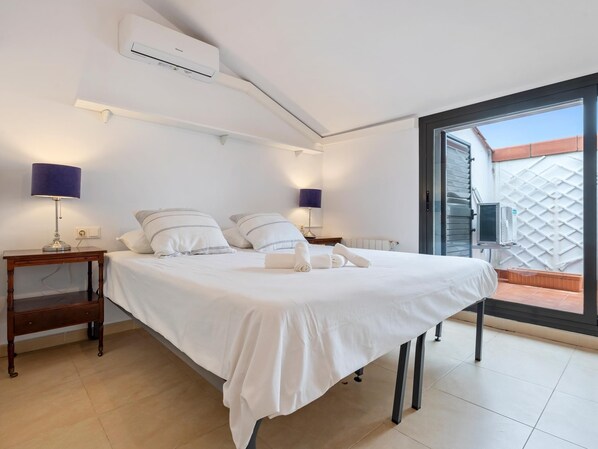 Un dormitorio con una cama, dos mesitas de noche, lámparas, un equipo de aire acondicionado y un ventanal corredero a un espacio exterior.