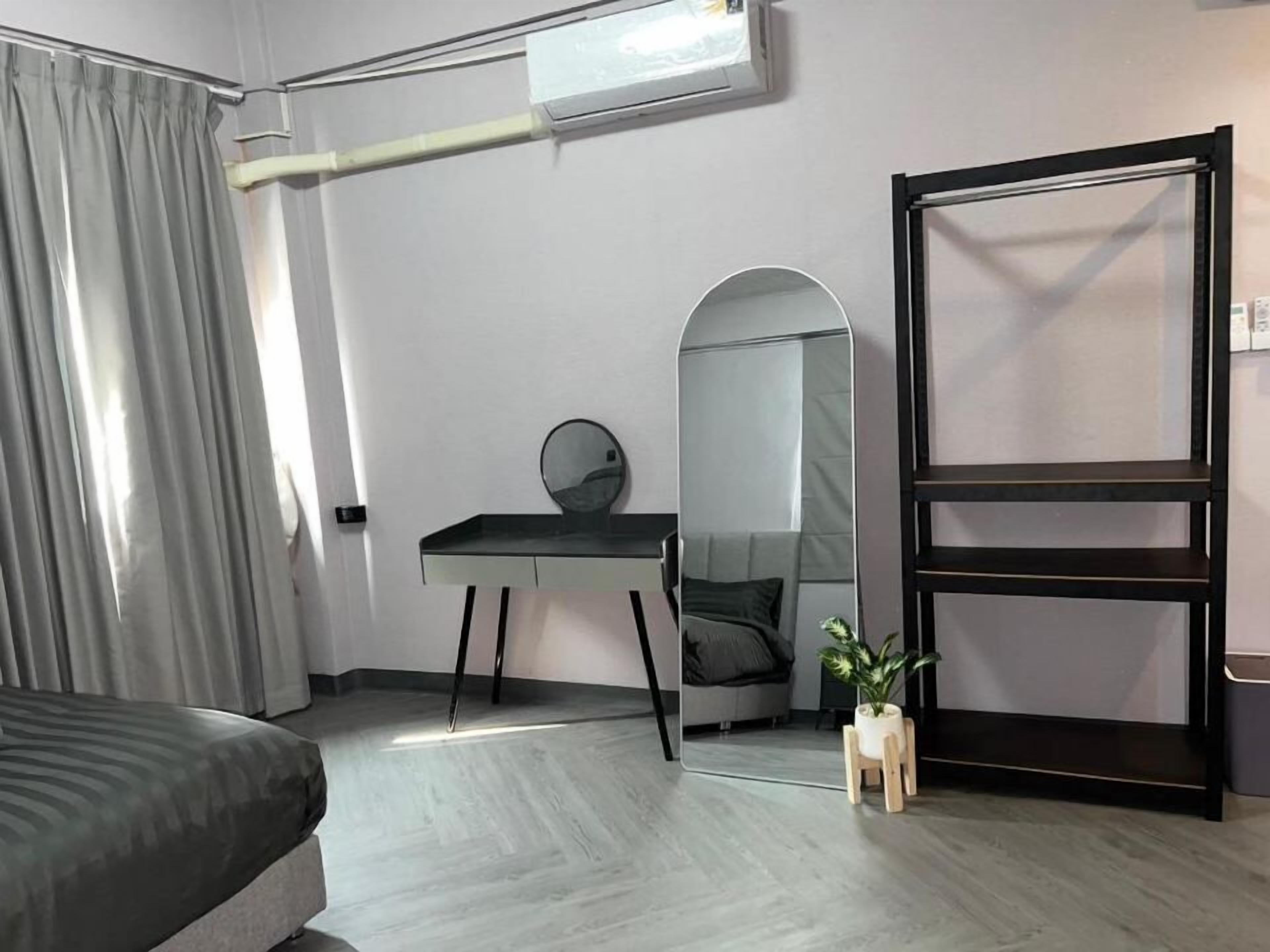 Une chambre moderne comprenant un lit, un bureau avec un miroir, un grand miroir, une plante et une armoire noire.