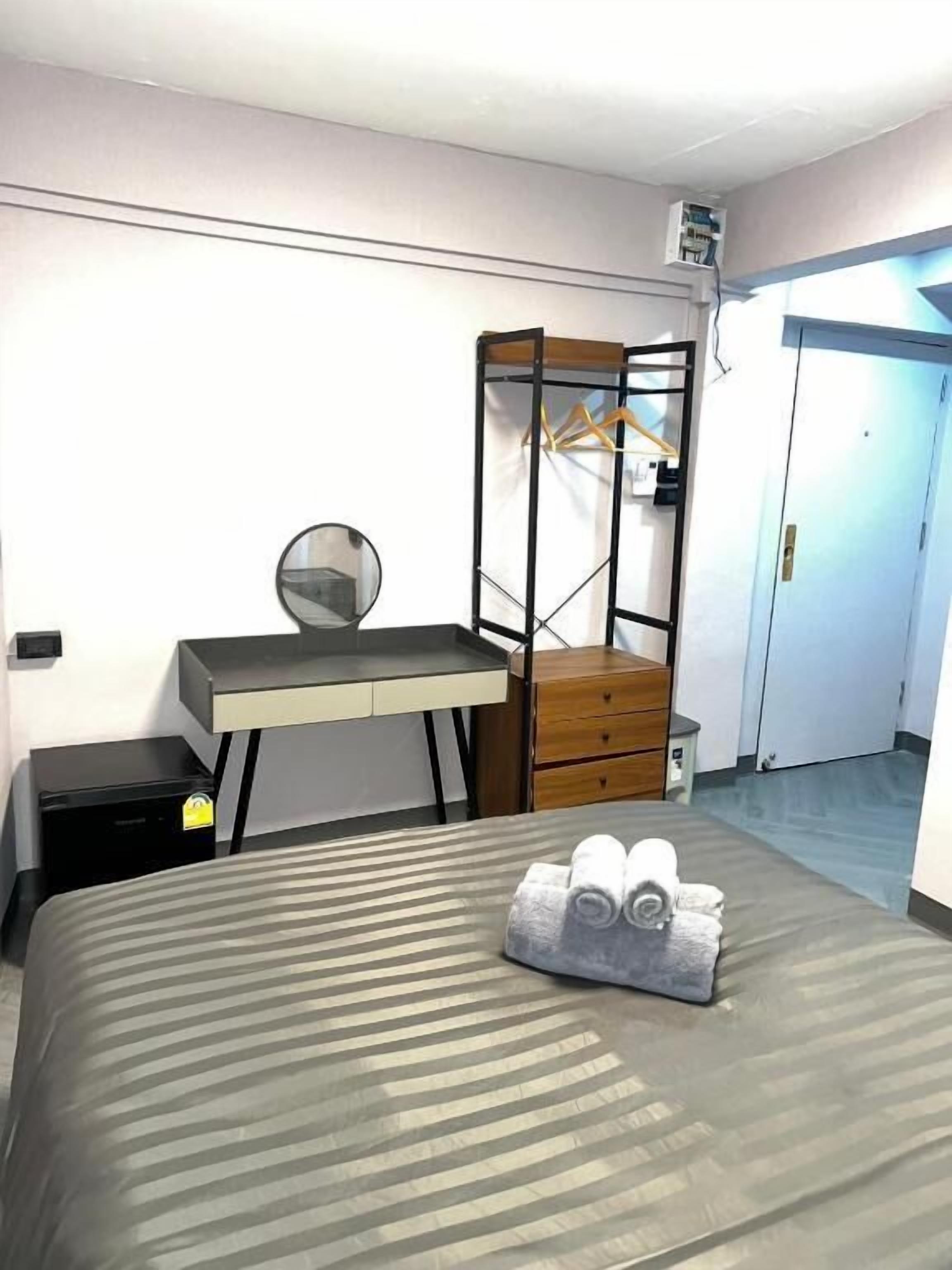 A bedroom with a bed, a desk, a mirror, a wardrobe, and a hanging rack.