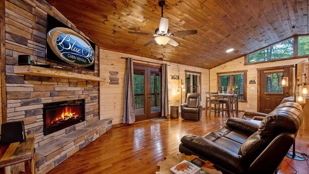 Eine Hütte mit Kamin aus Stein, Ledersofa, Holzböden und Deckenventilator.