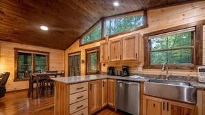 Ein Holzblockhaus-Interieur mit Küche, Essbereich und großen Fenstern.