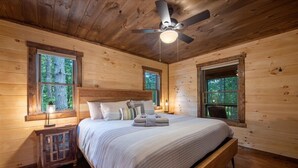 Ein Schlafzimmer einer Holzhütte mit Bett, Fenstern, Deckenventilator und Nachttisch.