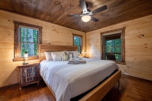 A wooden cabin bedroom with a bed, windows, a ceiling fan, and a nightstand. - Brew Ridge | Blue Ridge, Ga (Blue Ridge)