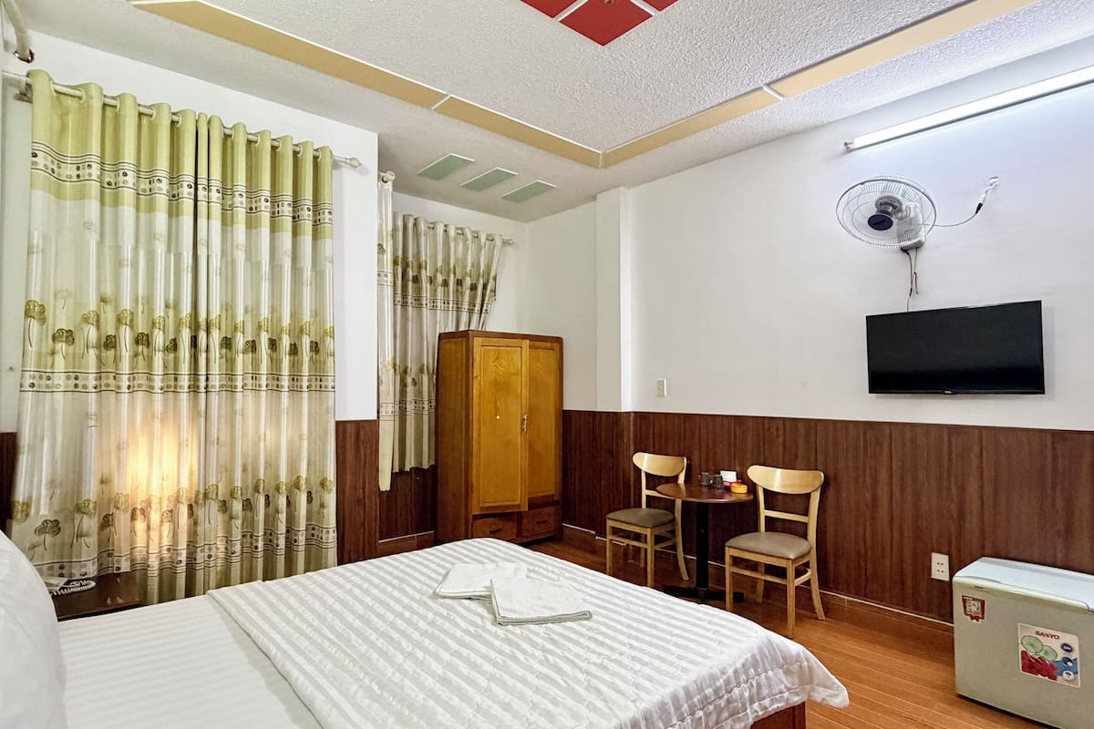 Una habitación de hotel con cama, un armario de madera, un televisor fijado en la pared y una pequeña mesa con sillas.