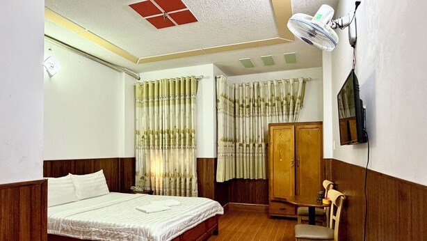 A bedroom with a wooden bed, a wardrobe, a desk with a chair, and a television mounted on the wall. - Hoa Nang Mai Hotel (Ho Chi Minh City)