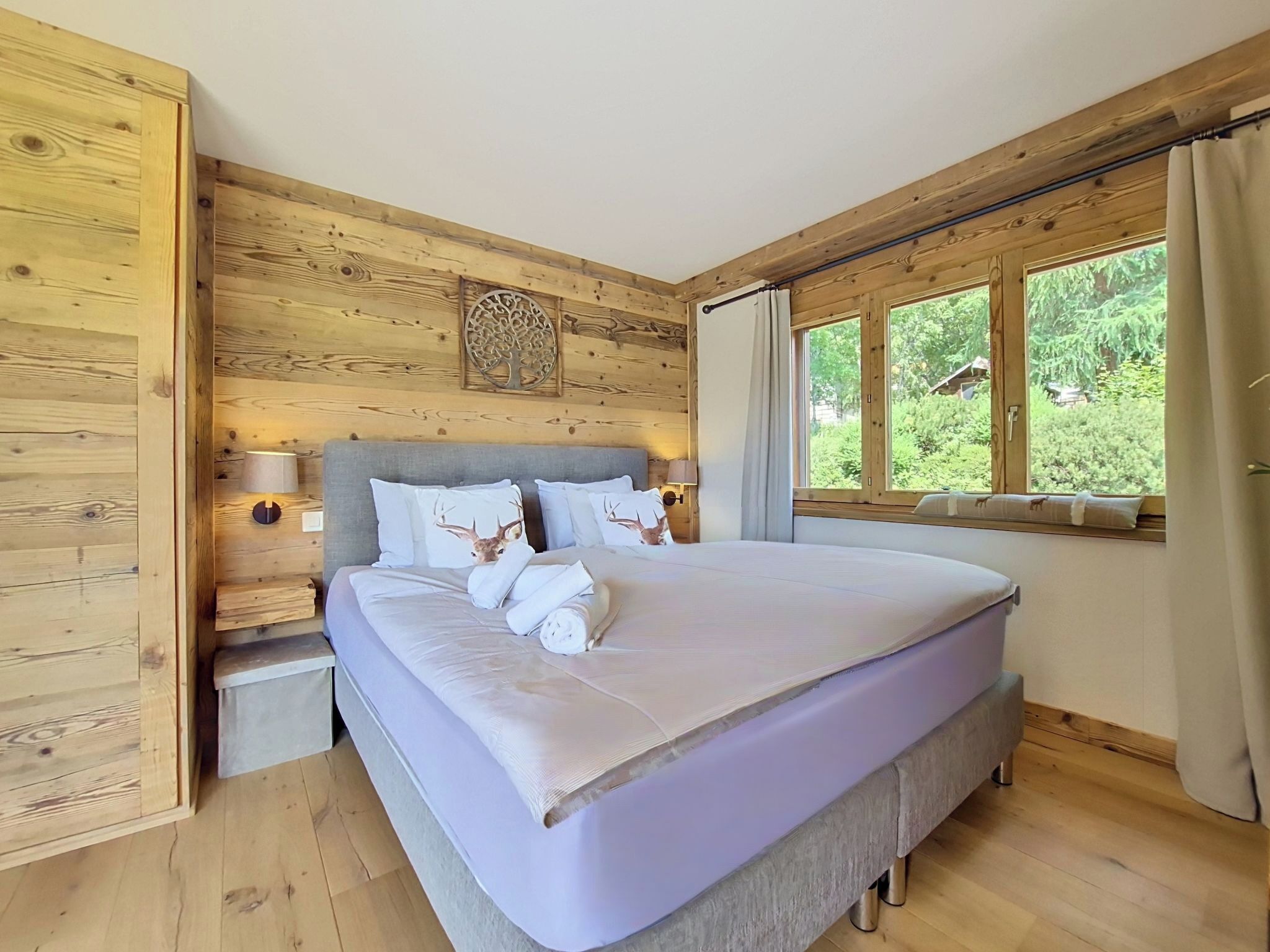 A wooden-paneled room with a bed, a window with curtains, and a wall-mounted light fixture.