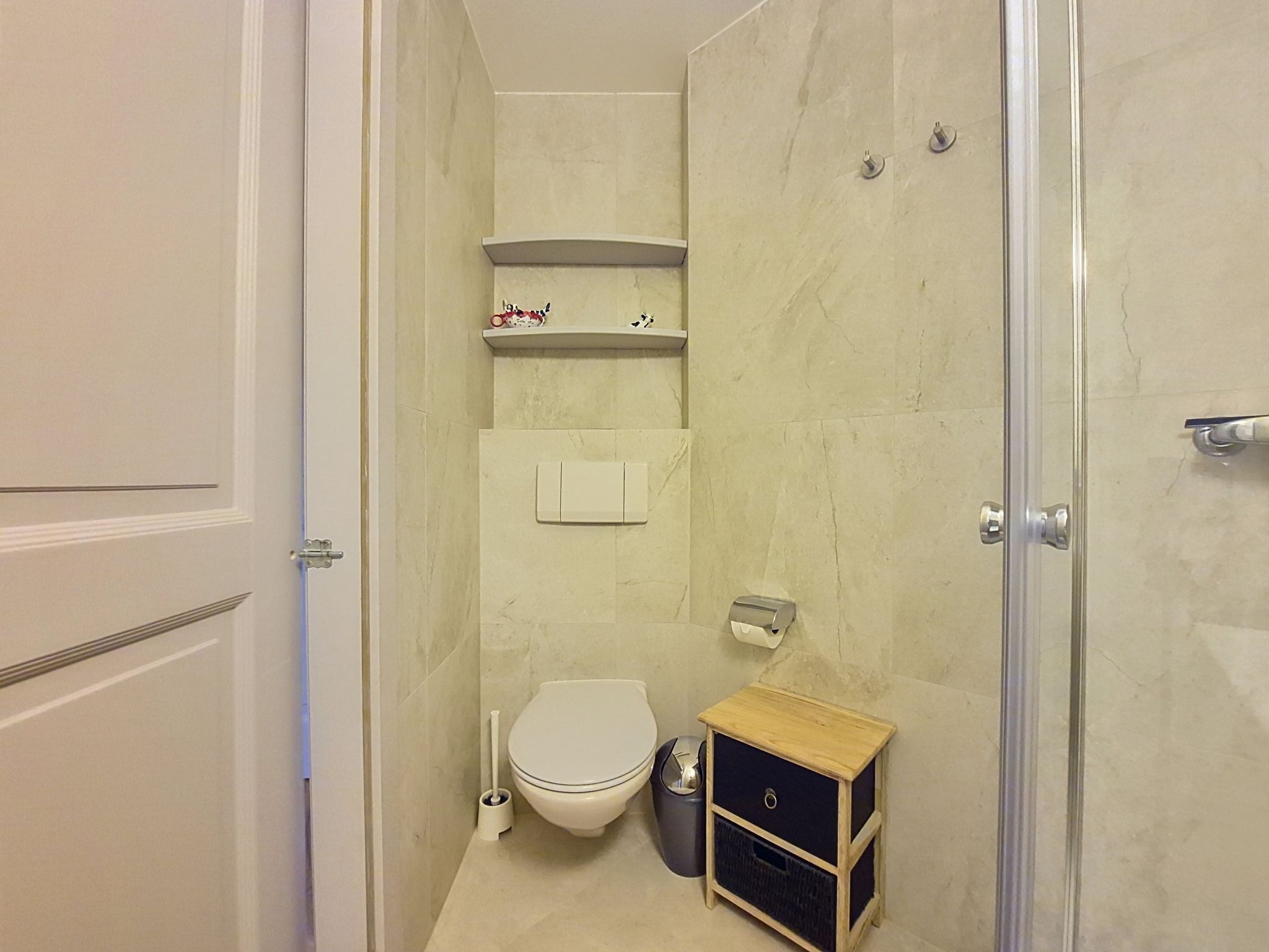 Ein kleines Badezimmer mit Toilette, einem Wäschekorb, einer Ablage für Pflegeprodukte und einer Duschkabine.