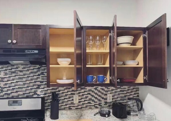 Une cuisine avec un mur recouvert de carreaux, une cuisinière et des placards ouverts contenant de la vaisselle et des verres.