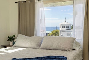 Ein Bett mit weißer Bettdecke, einer blauen Tagesdecke und Blick auf ein Gebäude mit Kuppel und einem Schild, auf dem 'Hotel de la Mer' steht.