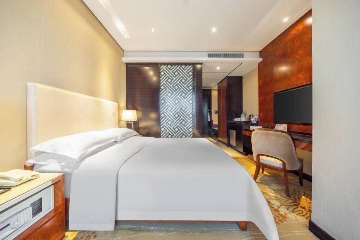 A hotel room with a bed, a desk, a chair, a TV, and a bathroom visible through a door.