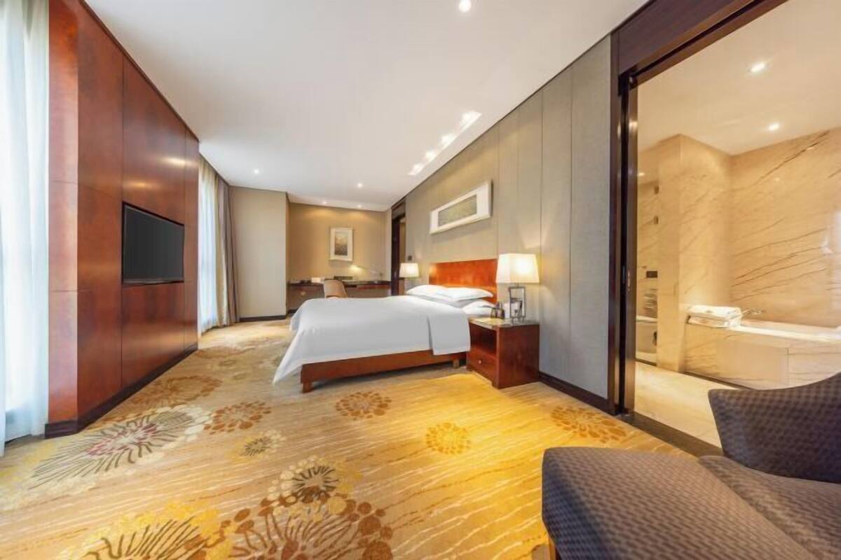 A hotel room with a bed, a TV, a bathroom with a marble wall, and a patterned carpet.