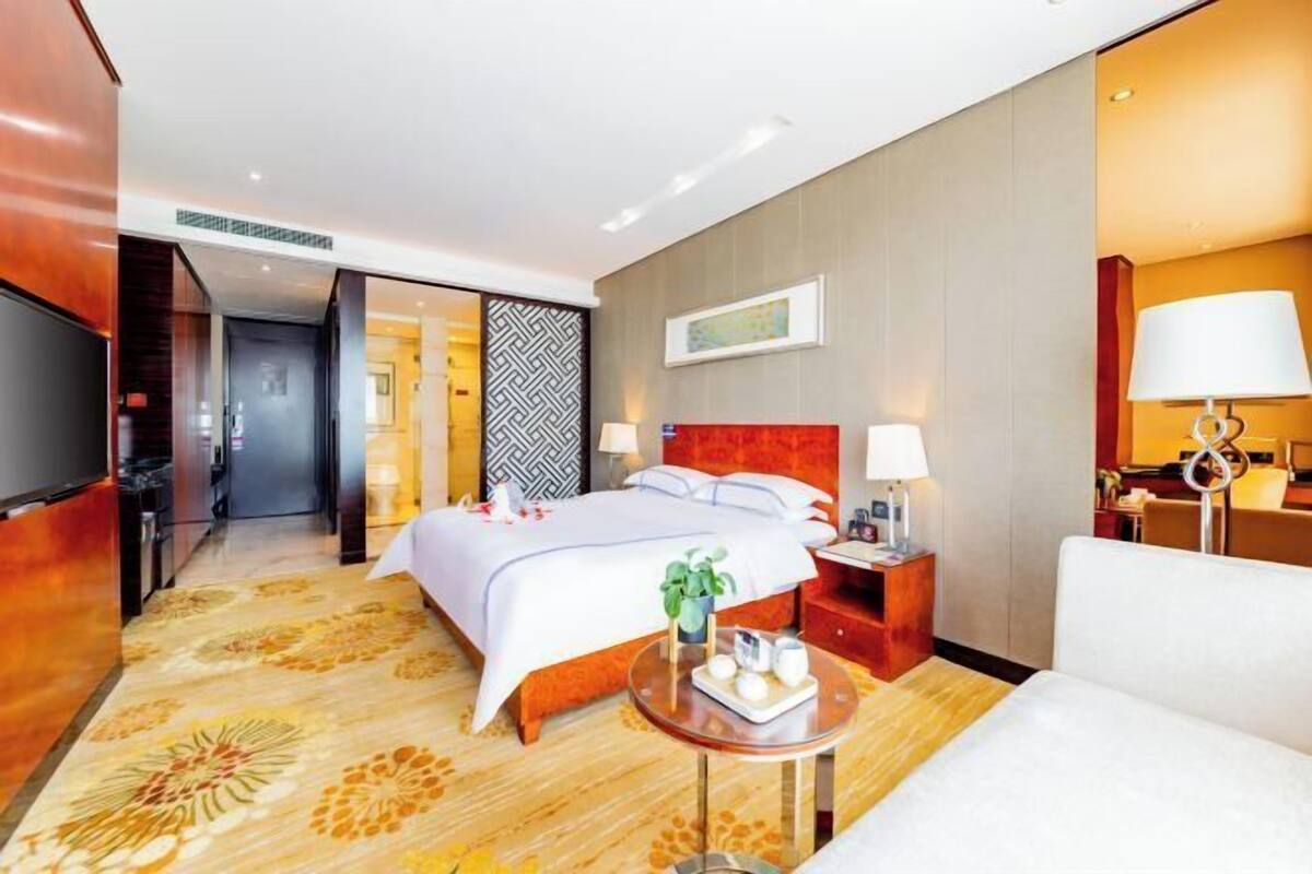 A hotel room with a bed, bedside tables, a TV, a sofa, and a decorative rug.