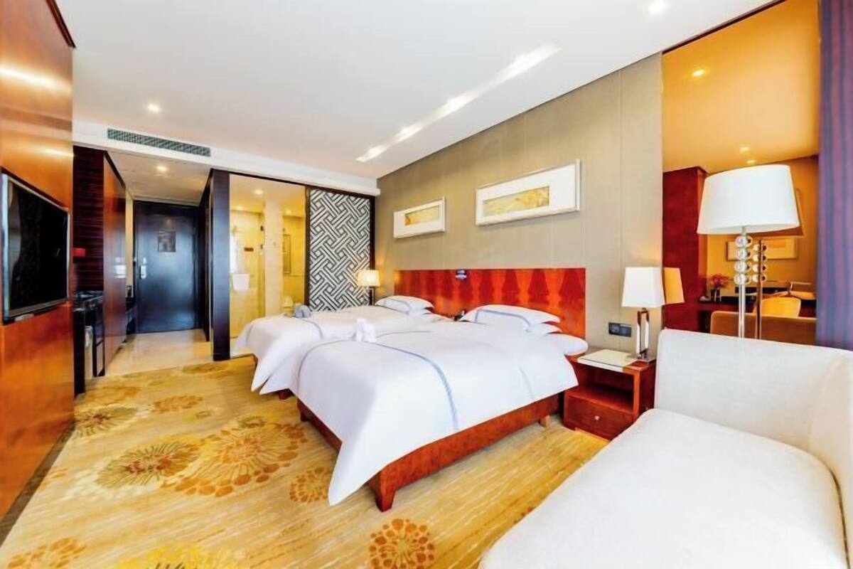 A hotel room with a large bed, a desk, a chair, a TV, and a bathroom visible through an open door.