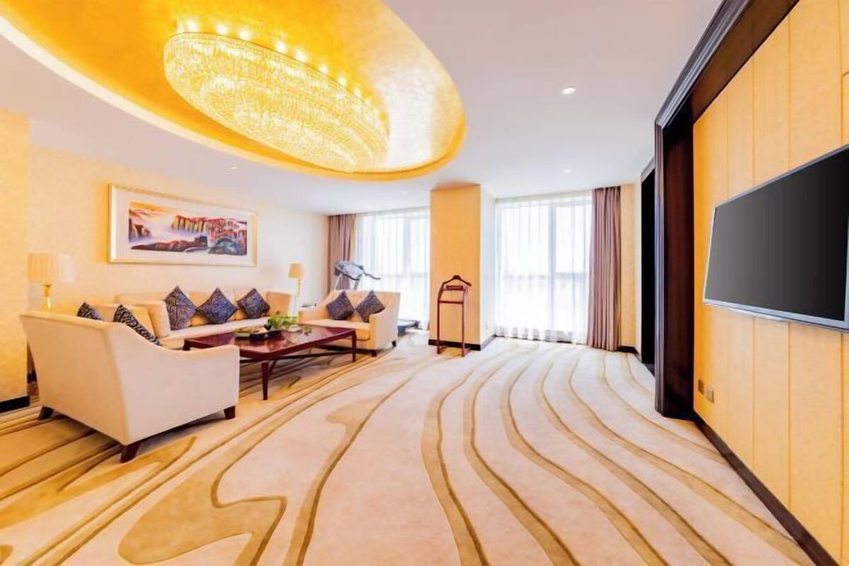 A hotel room with a sofa, armchair, and a flat-screen TV.
