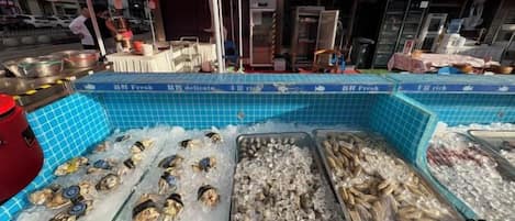 Mostrador de mercado con mariscos frescos sobre hielo y un paraguas rojo.