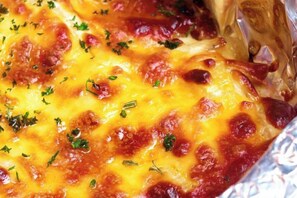 A close-up of a baked dish with melted cheese and herbs. - The Royal International Hotel (Ordos)