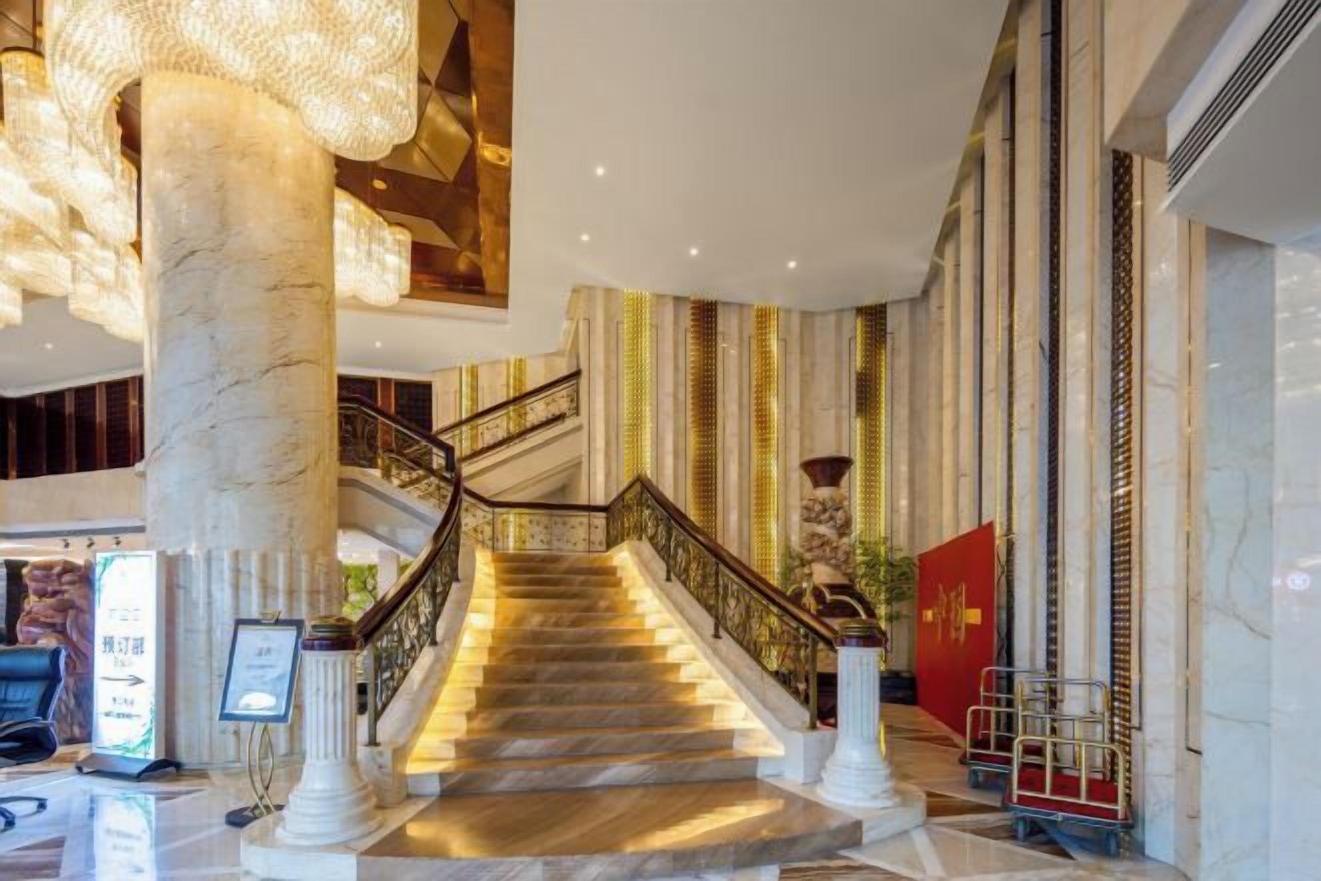 Una imponente escalera con columnas de mármol y una bandera roja que conduce a un vestíbulo con techos altos y un candelabro.