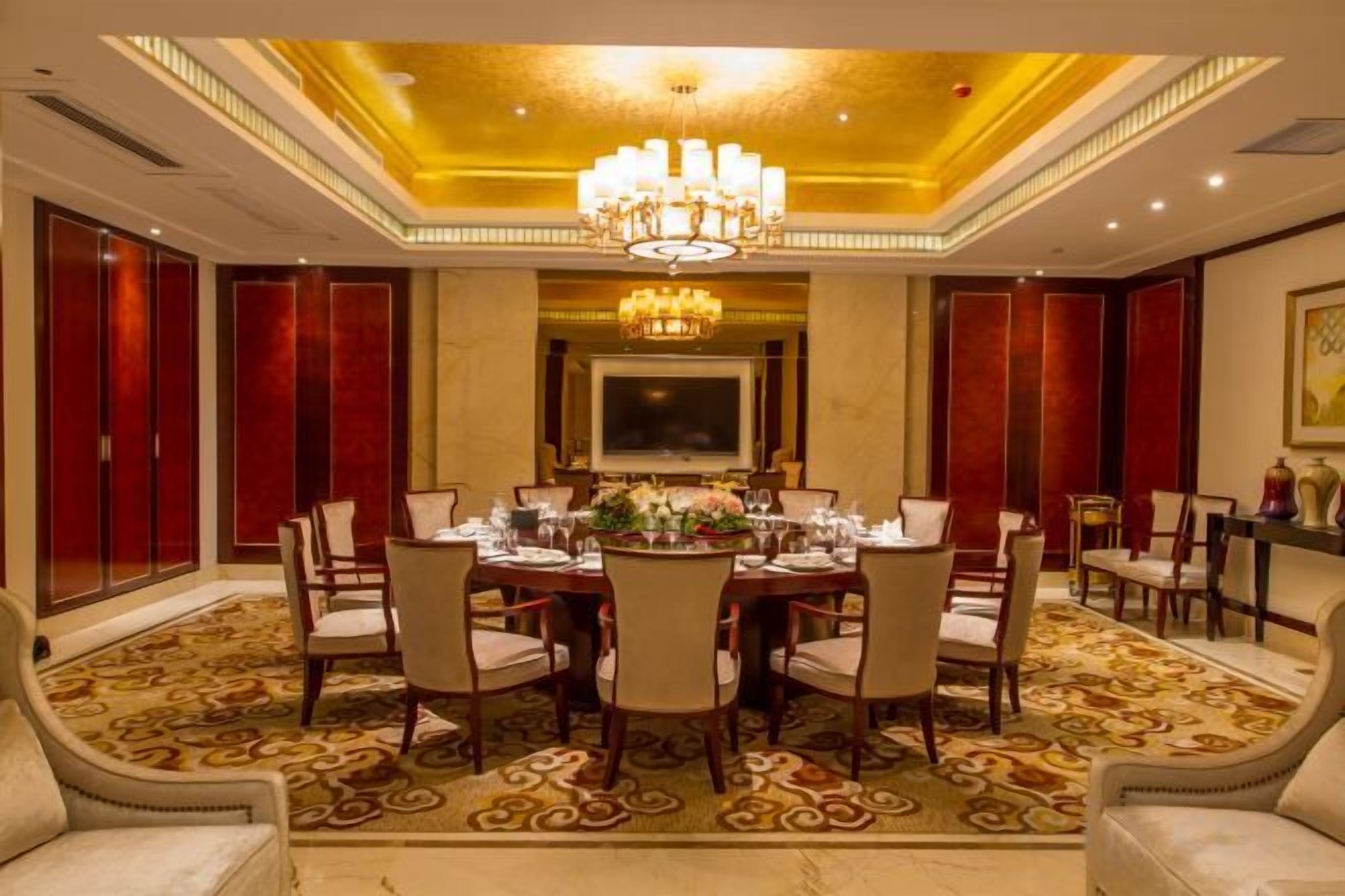 A formal dining room with a chandelier, a large table set for six, and red paneling on the walls.