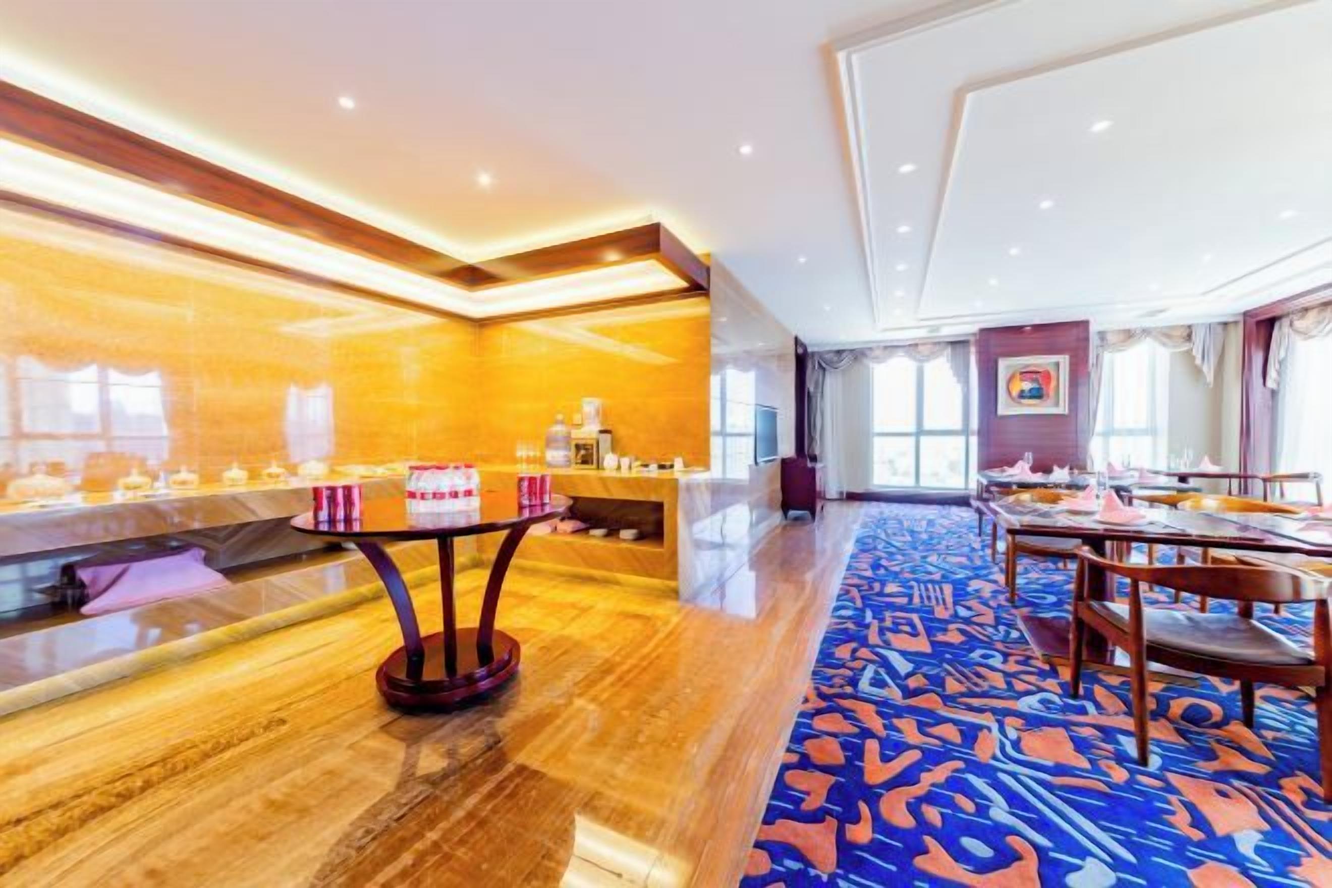 Un vestíbulo de hotel con una recepción, una larga mesa de comedor con sillas y una alfombra estampada.