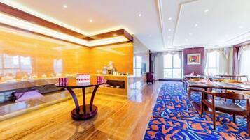 Un vestíbulo de hotel con una recepción, una larga mesa de comedor con sillas y una alfombra estampada.