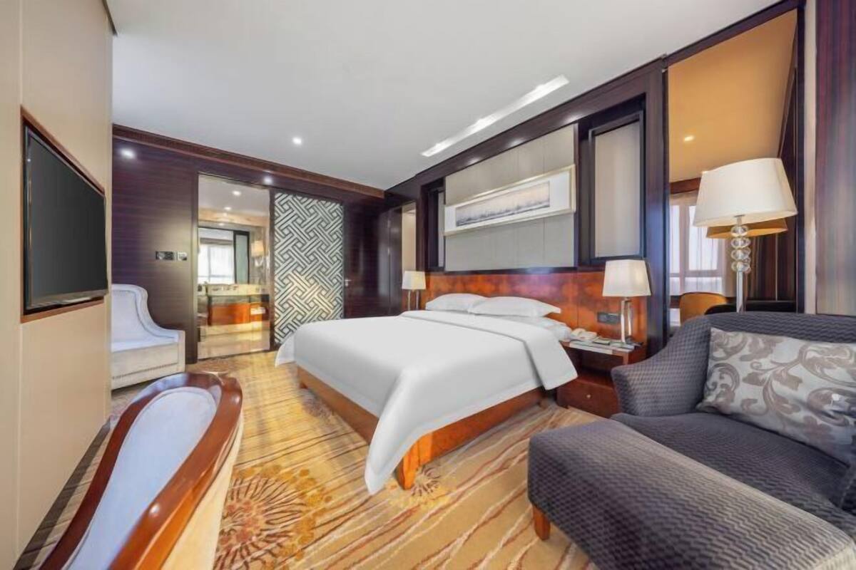 A hotel room with a large bed, a sofa, a TV, and a bathroom with a bathtub.