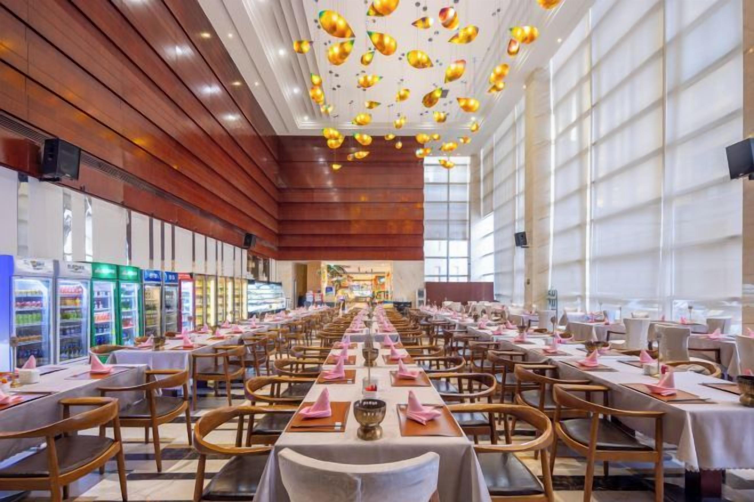 A spacious dining area with multiple tables and chairs, a long counter, and a high ceiling with hanging lights.